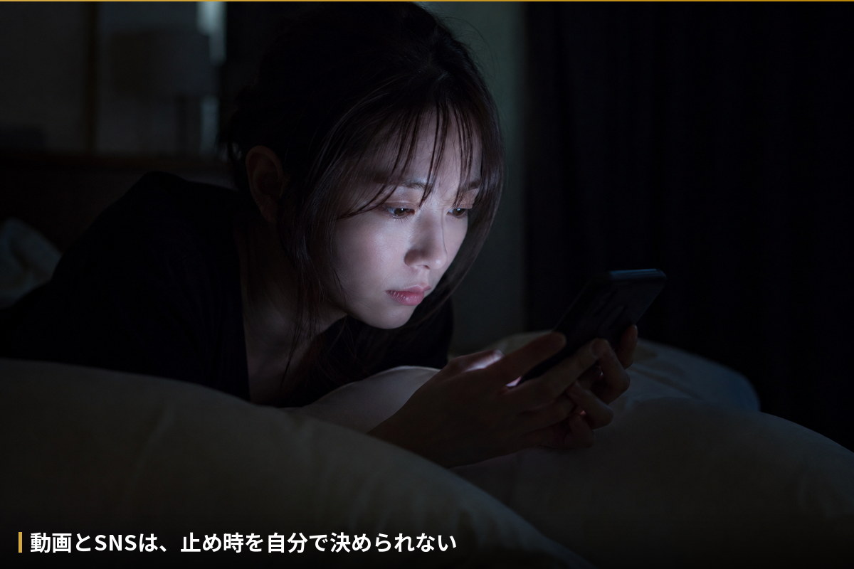 暗い寝室でスマホの光だけが顔を照らしている様子